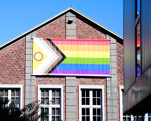 Ein Backsteinhaus ist zu sehen, das eine Regenbogenfahne ziert