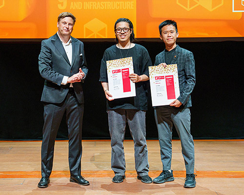 Drei Personen stehen auf einer Bühne und halten Urkunden in den Händen