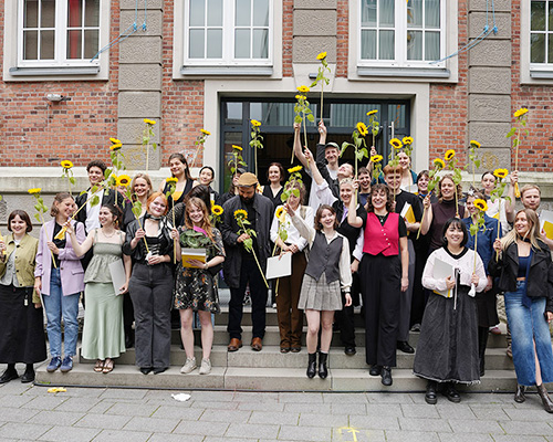 Eine Gruppe Menschen mit Sonnenblumen in den H&auml;nden posiert f&uuml;r ein Gruppenfoto
