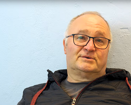 Ein Mann in Arbeitskleidung sitzt vor einer Wand