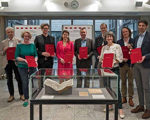 Neun Personen stehen mit Urkunden in den H&auml;nden in einer Bibliothek