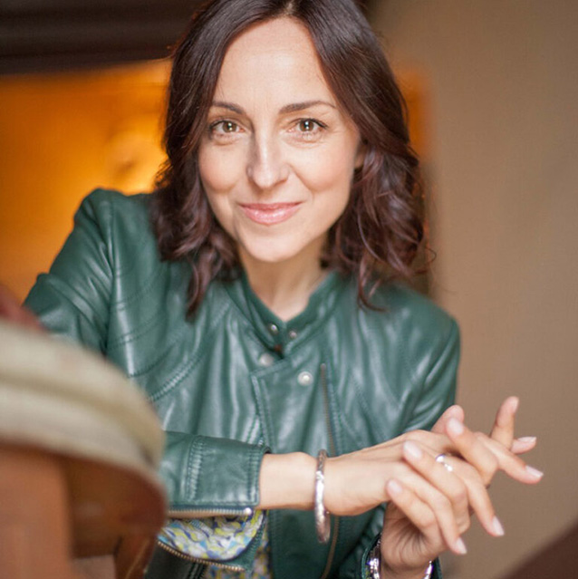 Eine dunkelhaarige Frau schaut mit gefalteten H&auml;nden in die Kamera