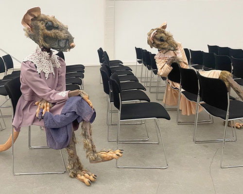 Foto aus einem Ausstellungsraum, in dem M&auml;usefiguren auf St&uuml;hlen sitzen