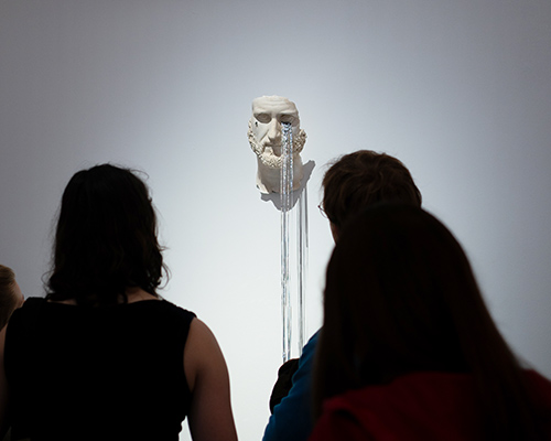 Foto aus einem Ausstellungsraum, in dem zwei Personen eine Figur betrachten