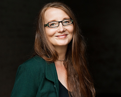 Die Schriftstellerin Emma Braslavsky posiert mit offenem Haar und Brille vor einem schwarzen Hintergrund.
