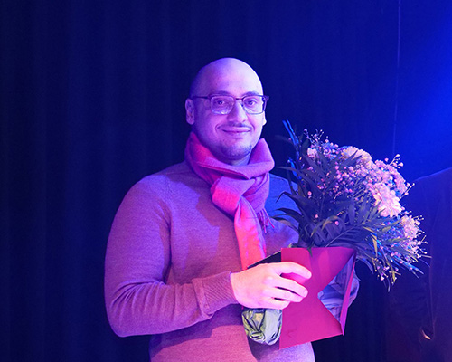 Das Bild zeigt Gor Margaryan, der einen Blumenstrauß und eine Auszeichnung des Filmfests in den Händen hält.