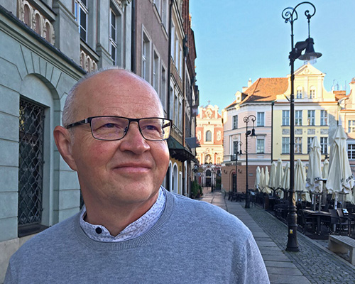 Ein Mann steht auf dem Gehweg einer Stadt und lässt sich fotografieren