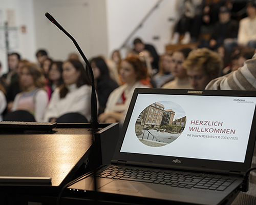 Viele Personen sitzen im Zuschauerraum, ein Laptop steht im Vordergrund